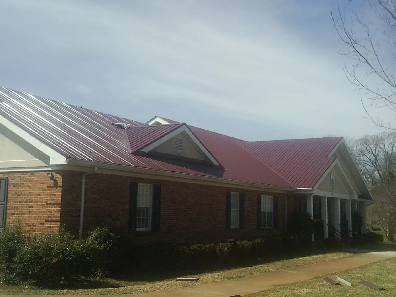 Red metal roof with gabled entries on a long brick building, from a Hail Damage Roof Repair job in Laguna Beach